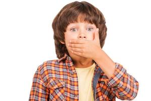 Oops Frustrated little boy covering mouth with hand and looking at camera while standing isolated on white photo