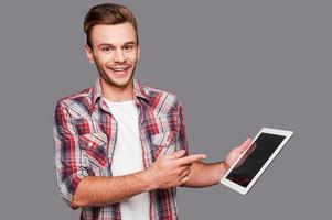 Your advertisement may be here Cheerful young man holding a digital tablet and pointing it while standing against grey background photo