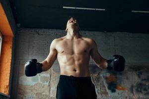 joven furioso con guantes de boxeo gritando mientras está de pie en el gimnasio foto