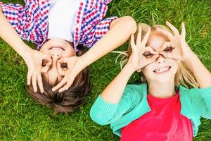 Summer fun. Top view of two cute little children making faces and smiling while lying on the green grass together photo