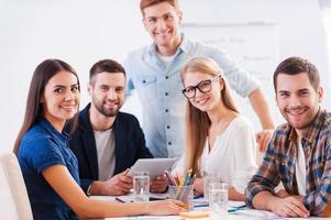 Ready to brainstorm. Group of happy business people in smart casual wear sitting together at the table and looking at camera photo