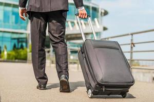 Ready to business trip. Rear view of businessman in formalwear carrying suitcase while walking away photo