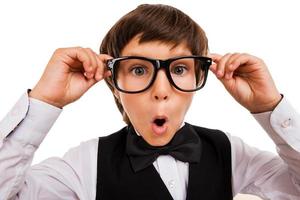 Wow Surprised little boy keeping mouth open and adjusting his glasses while standing isolated on white photo