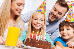 feliz cumpleaños familia feliz de cuatro celebrando el cumpleaños de una niña feliz sentada en la mesa con pastel de cumpleaños foto