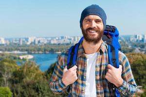 turista confiado. un joven apuesto que lleva una mochila y mira la cámara a través de los hombros con una sonrisa foto