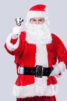 Merry Christmas Traditional Santa Claus ringing a bell and looking at camera while standing against grey background photo
