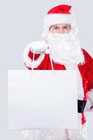 This is for you Traditional Santa Claus stretching out hand with shopping bag while standing against grey background photo