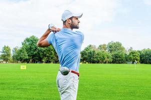 Great strike. Side view of confident golfer swinging his driver and looking away while standing on golf course photo