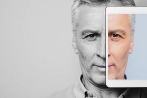 Live a colorful life. Black and white portrait of confident senior man with digital tablet covering half face photo