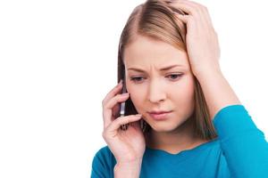 Not ready for this talk. Beautiful young women talking on the mobile phone and touching her head while standing against white background photo