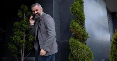 an adult businessman talking on a mobile phone enters turning around the business center building photo