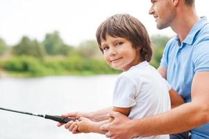 Fishing with my father. Cheerful father and son fishing together while little boy looking at camera and smiling photo