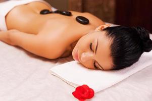 Enjoying stone SPA. Top view of beautiful young shirtless woman lying on massage table and keeping eyes closed with spa stones on her back photo