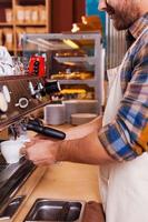 Barista at work. Side view of confident barista making coffee while standing at the bar counter near the coffee machine photo