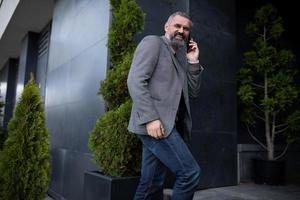 an elderly man businessman enters an office building talking on a mobile phone looking around with a smile photo