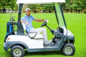 Man driving golf cart. Side view of handsome young man driving a golf cart and looking at camera photo