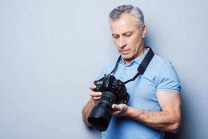 Setting the camera. Portrait of senior mature man in T-shirt holding camera while standing against grey background photo