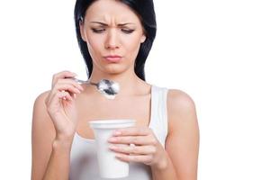 I hate diets Beautiful young woman holding a spoon with sour cream and making a face while standing against white background photo