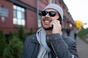 un hombre con una amplia sonrisa en la cara habla por teléfono móvil en la calle con gafas de sol foto