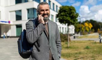 fifty year old businessman talking on the phone with a backpack on the background of an office building photo
