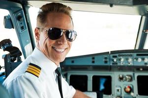 Pilot in cockpit. Rear view of confident male pilot looking over shoulder and smiling while sitting in cockpit photo