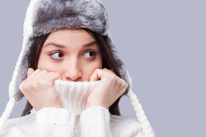 It is so cold. Frozen young women covering face with turtleneck while standing against grey background photo
