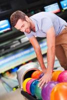 Choosing the lucky ball. Cheerful young man choosing bowling ball and smiling while standing against bowling alleys photo