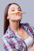 Crazy study. Happy young women holding pencil under her lips while standing against grey background photo