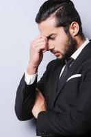 Breaking from the stress. Frustrated young man in formalwear touching head with fingers and keeping eyes closed while standing against grey background photo