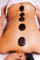 Hot stone therapy. Top view of young woman with shiny skin lying on front with spa stones on her back photo