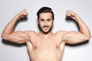 Strong man. Handsome young shirtless man keeping arms raised and looking at camera  while standing against grey background photo
