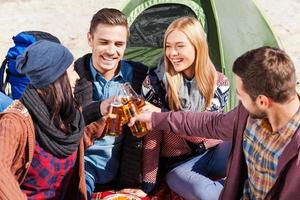 nos saluda la vista superior de cuatro jóvenes felices animando con cerveza y sonriendo mientras se sientan juntos cerca de la tienda foto