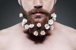 cuida bien tu barba primer plano de un joven sin camisa con flores en la barba de pie contra un fondo gris foto