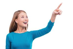 Over there Beautiful young woman pointing away and smiling while standing against white background photo