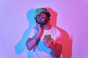 Handsome young man adjusting his headphones while enjoying music against colorful background photo