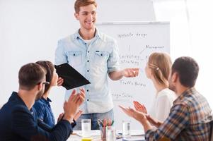 Great presentation Group of business people in smart casual wear sitting together at the table and applauding to their colleague standing near whiteboard and smiling photo