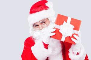 Merry Christmas and Happy New Year Traditional Santa Claus holding gift box and looking at camera while standing against grey background photo