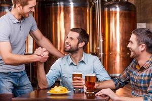 conociendo a un viejo amigo. tres jóvenes felices sentados juntos en un pub de cerveza mientras dos de ellos se dan la mano foto