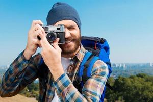 No puede faltar un paisaje tan hermoso. apuesto joven cargando mochila y tomando una foto de una vista