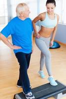 Do it this way. Full length of cheerful physical therapist working with senior man in health club photo