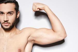 Perfect bicep. Close-up of muscular man showing his perfect bicep while standing against grey background photo