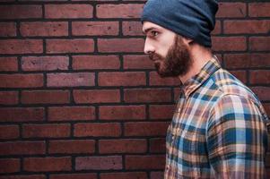 Confident handsome. Side view of handsome young bearded man standing against brick wall photo