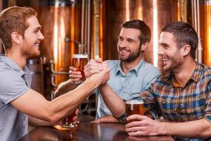 pasar un buen rato con amigos. tres jóvenes felices bebiendo cerveza de manera informal mientras se sientan juntos en un pub de cerveza foto