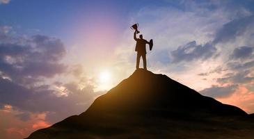 empresario de victoria con trofeo en la cima de la montaña. éxito, logro de objetivos, liderazgo, carrera, ganador y concepto de logro empresarial. foto