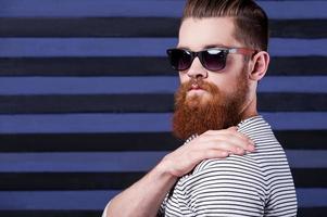 Casual confidence. Handsome young bearded man holding hand on shoulder while standing against stripped background photo