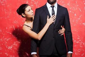Passion and desire. Cropped image of man in formalwear standing against red background while woman embracing him from behind photo