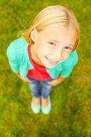 Curious little girl. Top view of cute little girl looking at camera and smiling while standing outdoors photo