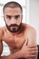 Portrait of masculinity. Confident young bearded man looking at camera while sitting indoors photo