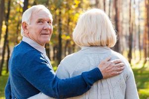 I love my wife. Rear view of happy senior man looking over shoulder and smiling while walking by park with his wife photo