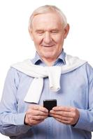 Technological wonders of nowadays. Happy senior man holding mobile phone while standing against white background photo